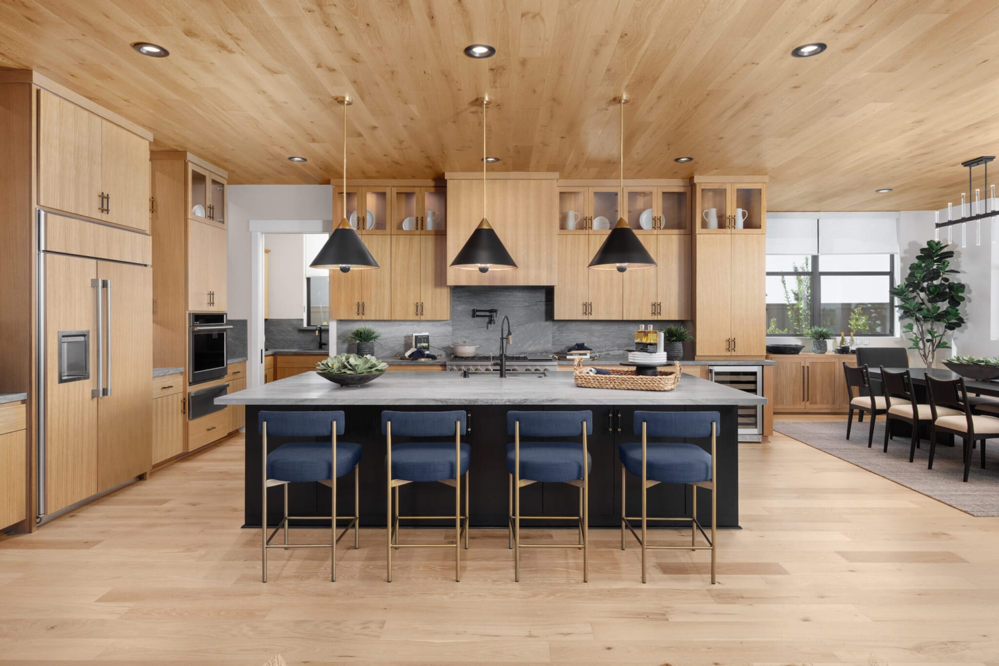 Luxury custom kitchen with natural oak cabinets, black island, navy counter stools and black pendant lights in Northern California