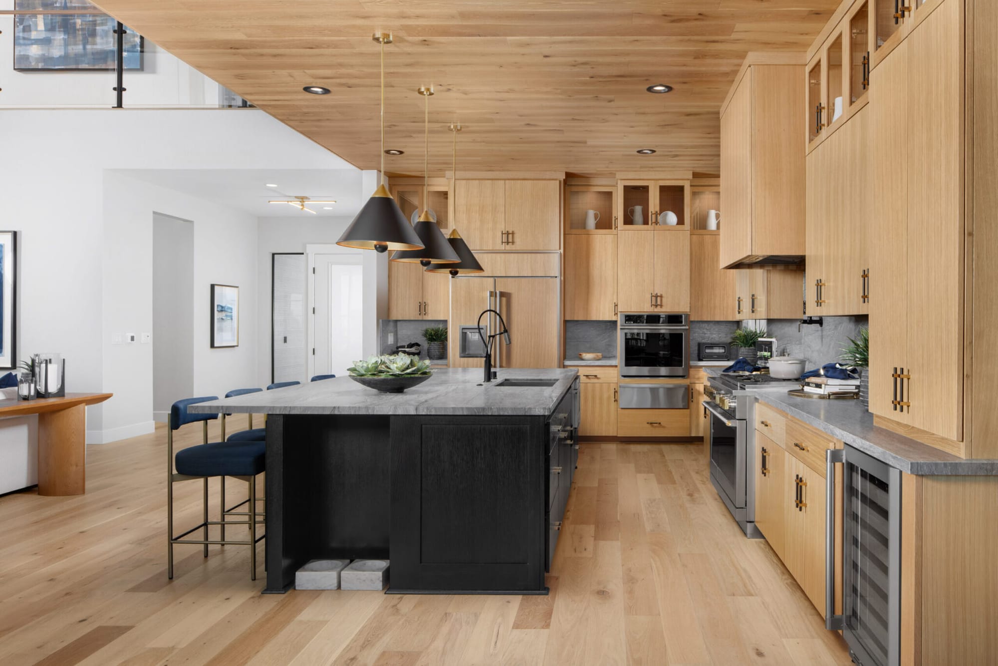 Light oak custom kitchen cabinets with black island, tall pantry wall and black pendant lights