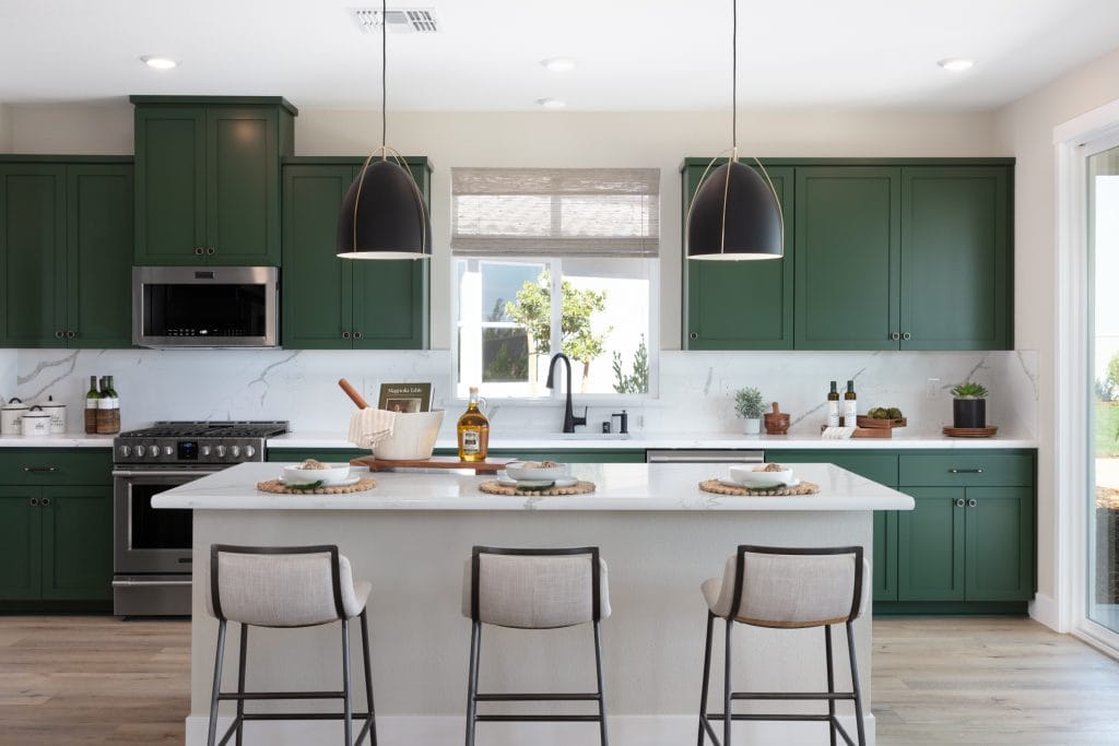 Painted forest green shaker kitchen cabinets with white quartz island and black dome pendants