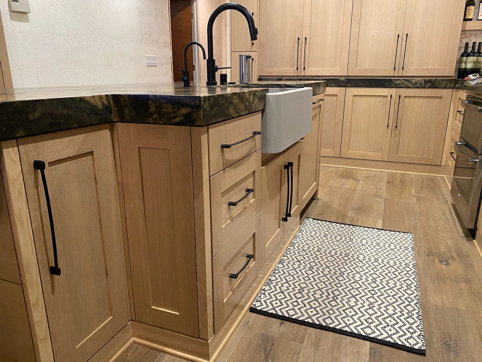 Tahoe Keys kitchen with custom white oak shaker cabinets, matte black pulls, farmhouse sink and green quartzite countertops