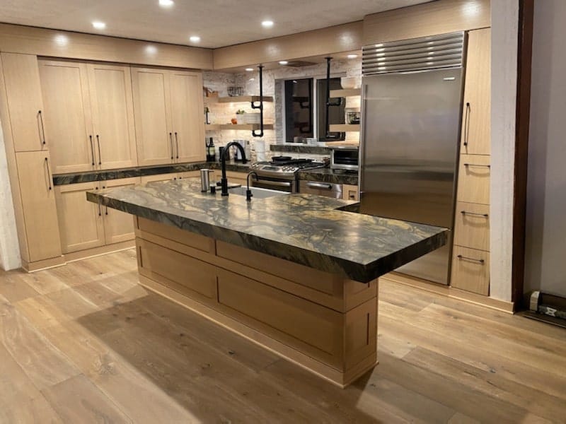 White oak kitchen island with green quartzite top and stainless Sub-Zero refrigerator in a Tahoe Keys home