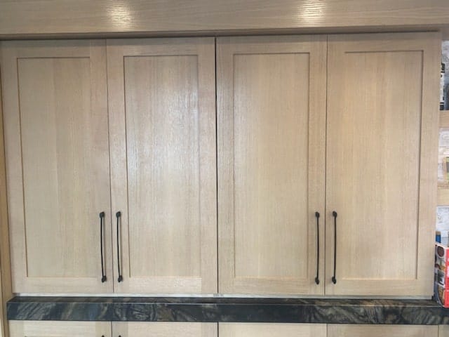 Wall of white oak shaker storage cabinets above a quartzite counter