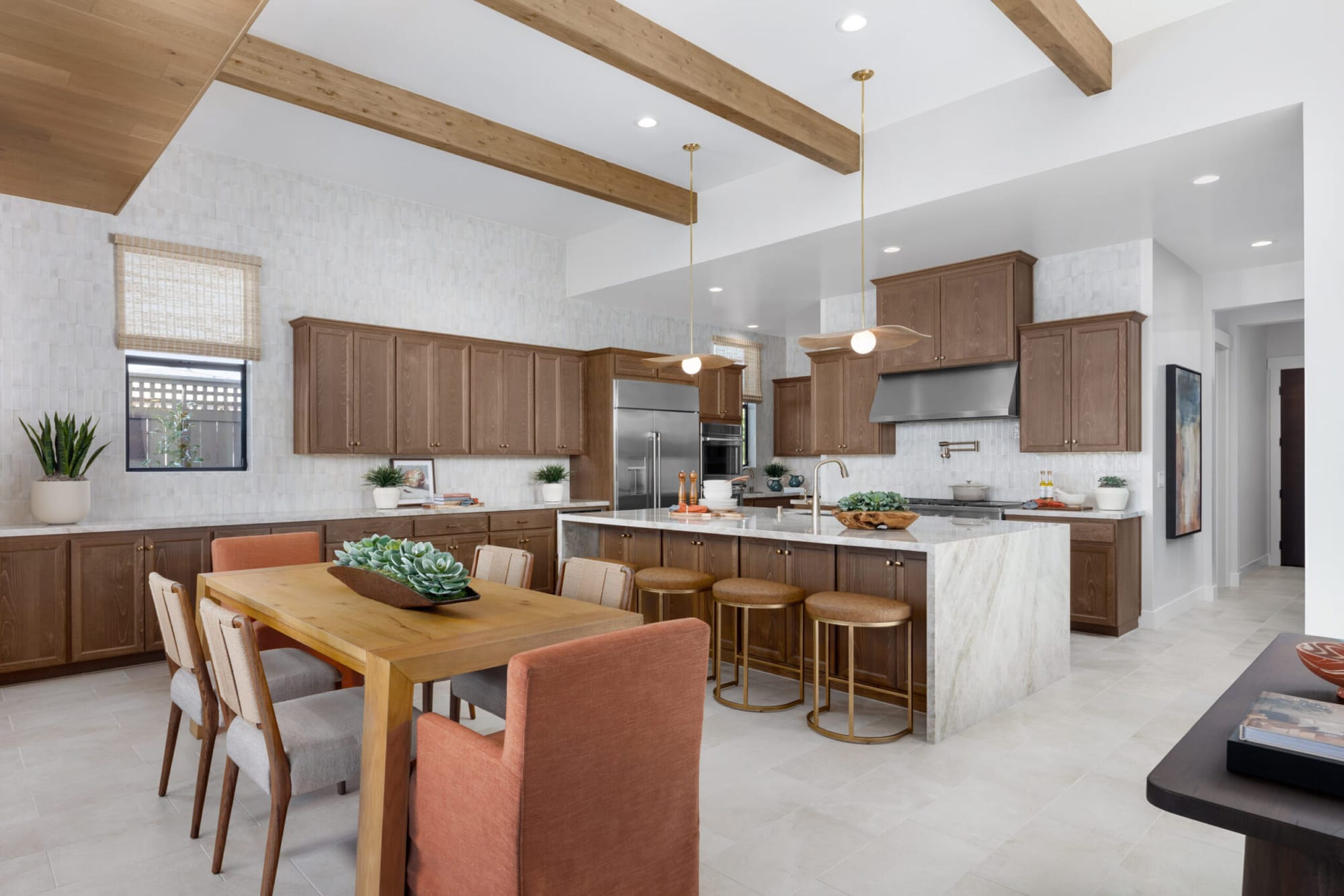 Medium stained kitchen cabinets under a beamed ceiling with waterfall island and dining table