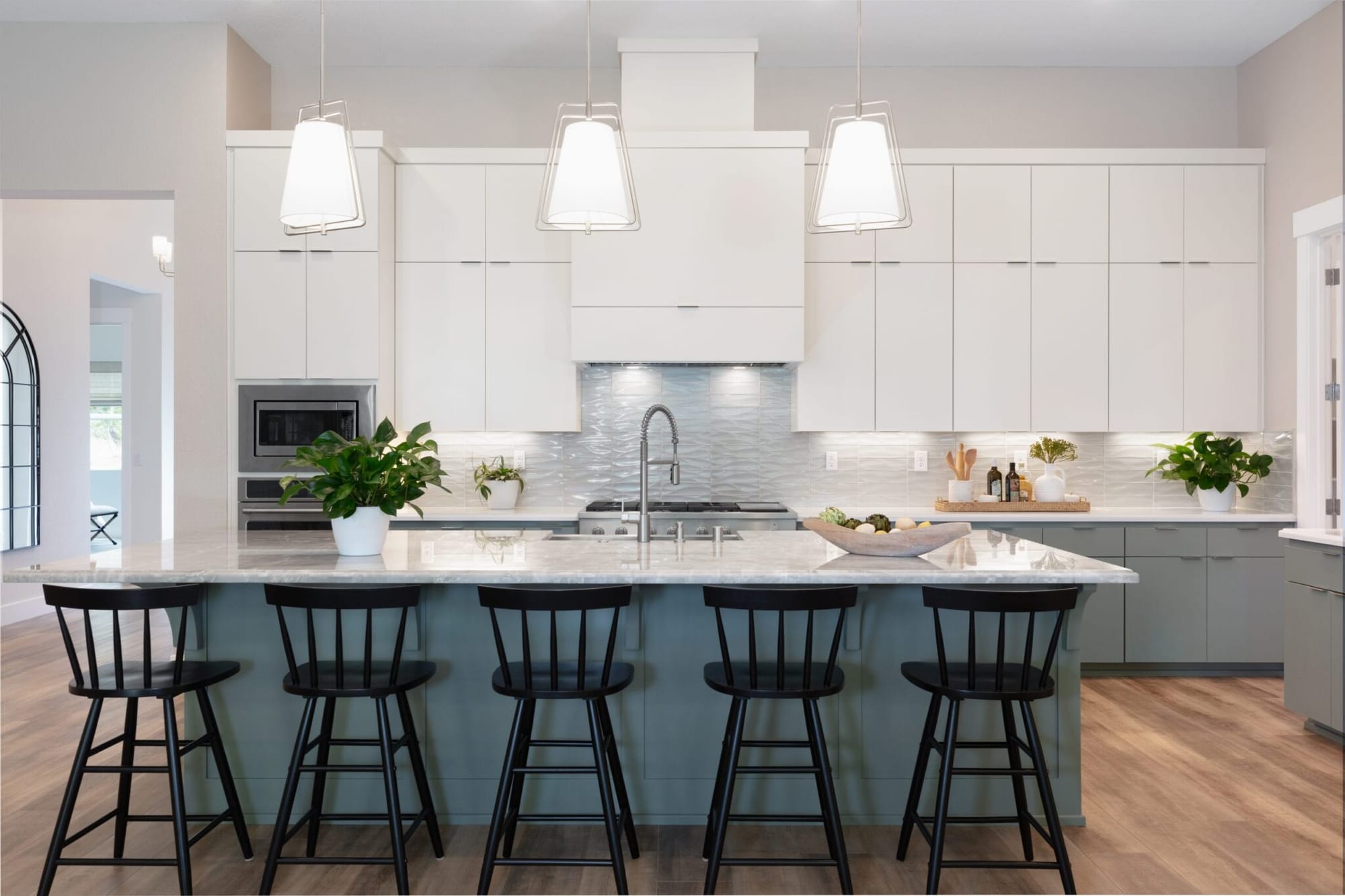 Interior designed kitchen with white custom cabinets, slate blue island, pendant lighting and black counter stools