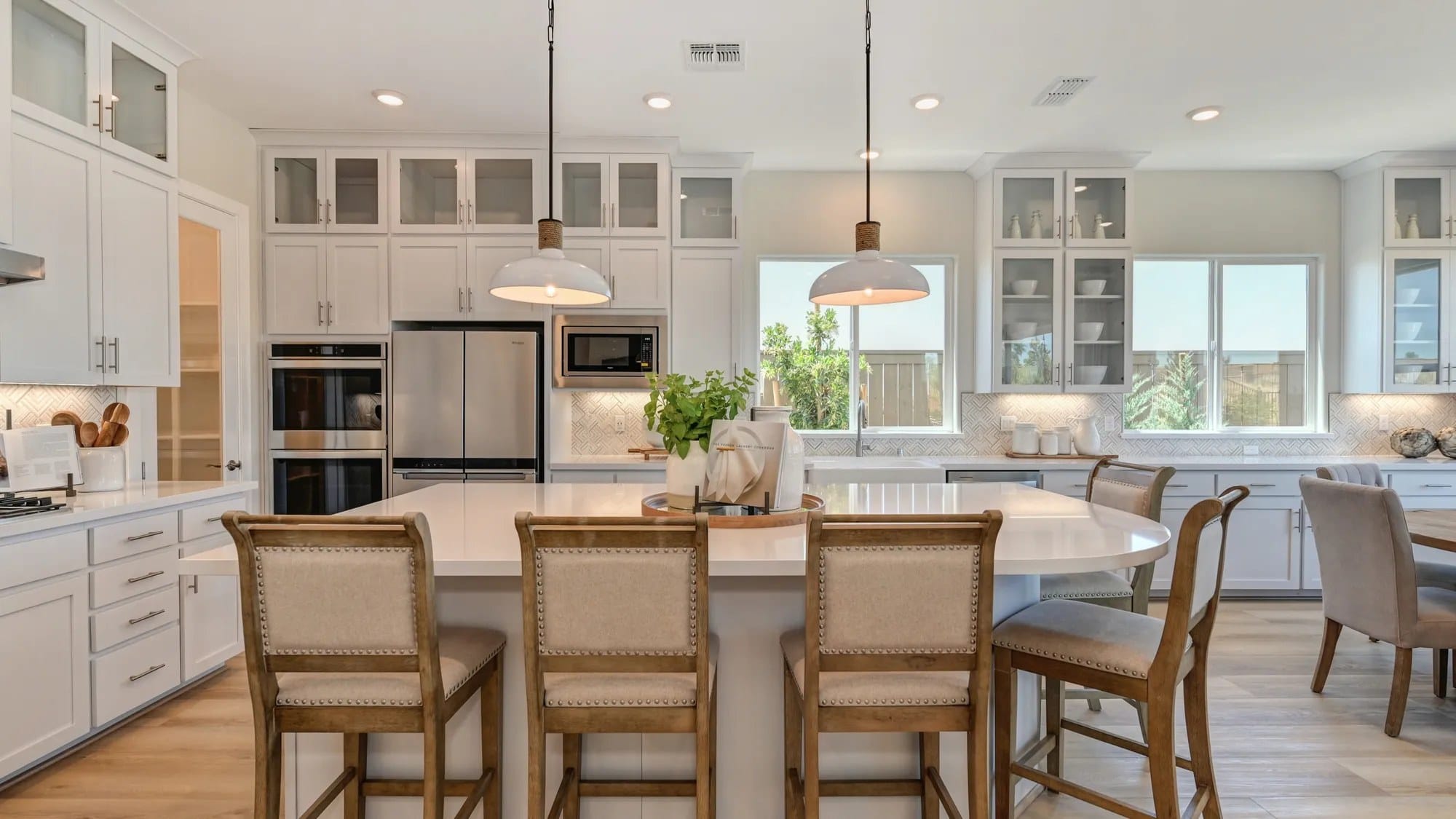 White shaker kitchen cabinets with glass-front uppers, double wall ovens and round island